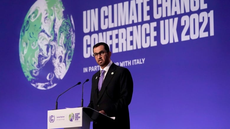 A man stands at a podium delivering an address. Behind him, a banner reads: UN Climate Change Conference UK 2021