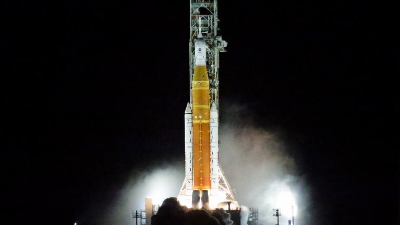 A rocket ship is seen launching from a pad against a dark sky.