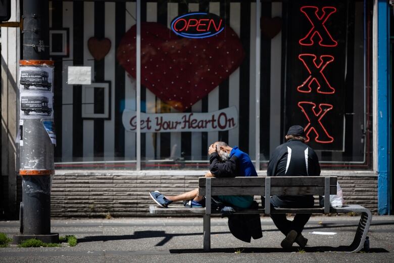 Two people sit on a bench in front of a sex shop display, with the words 'Get your heart on' and 'XXX