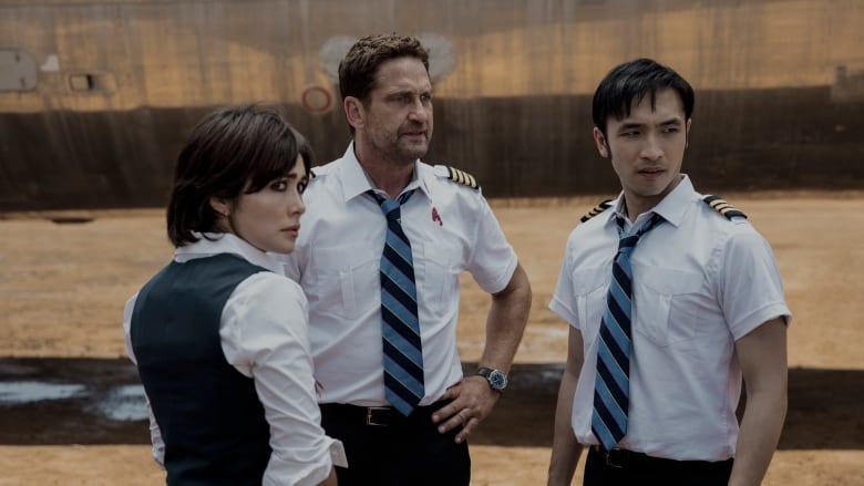 The flight crew try to decide their next move in a scene from Plane. From left to right, Daniella Pineda as the flight attendant Bonnie, Gerard Butler as Captain Brodie Torrance.  and Yoson An as co-pilot Dele. 