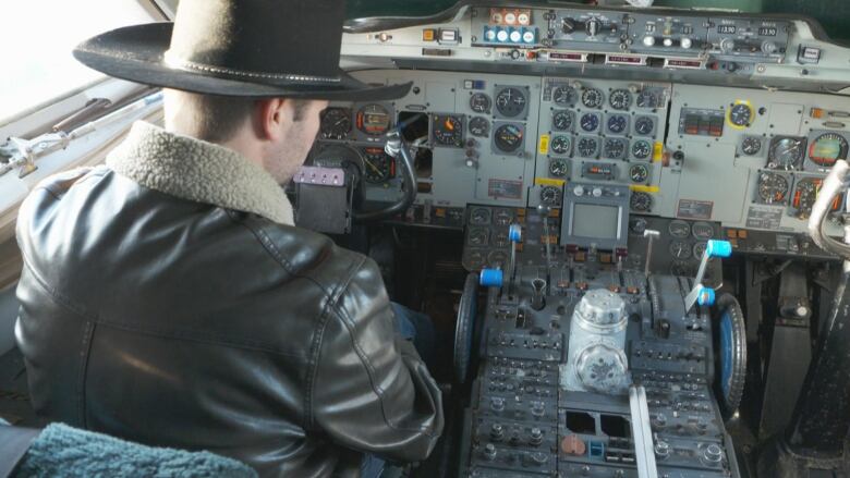 A man sits behind a massive control panel at the front of an airplane.