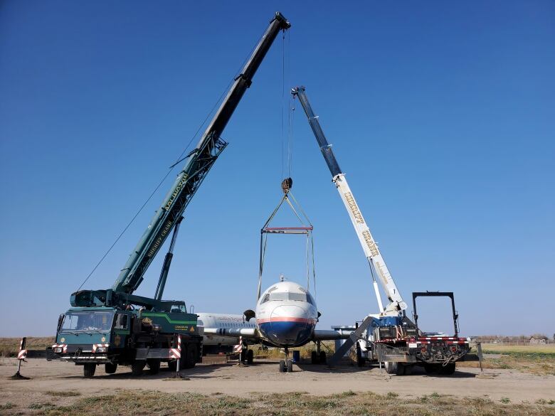 Two cranes sit on either side of an airplane.