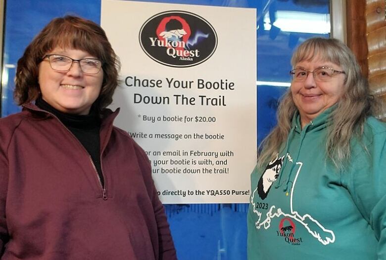 Two women stand in front of a Yukon Quest sign.