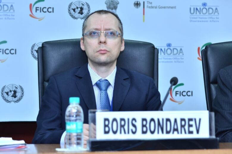 A man in a suit and glasses sits at an official desk behind a name plate that says Boris Bondarev. 