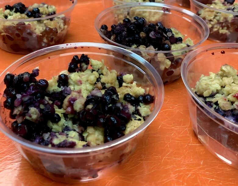 A plastic cup of blueberry crisp sits on an orange table.