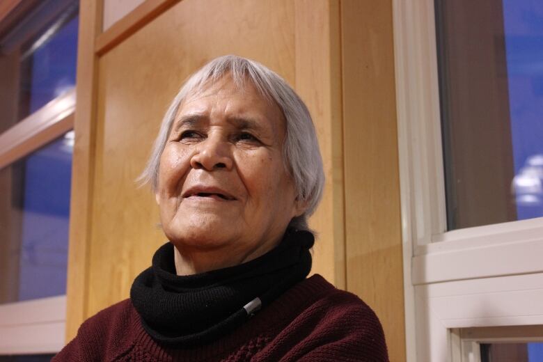 Head shot of a woman with short grey hair, a maroon sweater and a black neck warmer. 