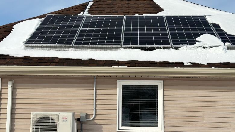 A house with solar panels on the roof and a heat pump on the ground. 