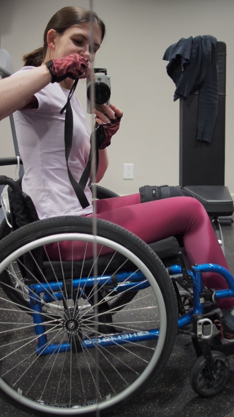 A woman in a wheelchair takes a selfie at the gym.