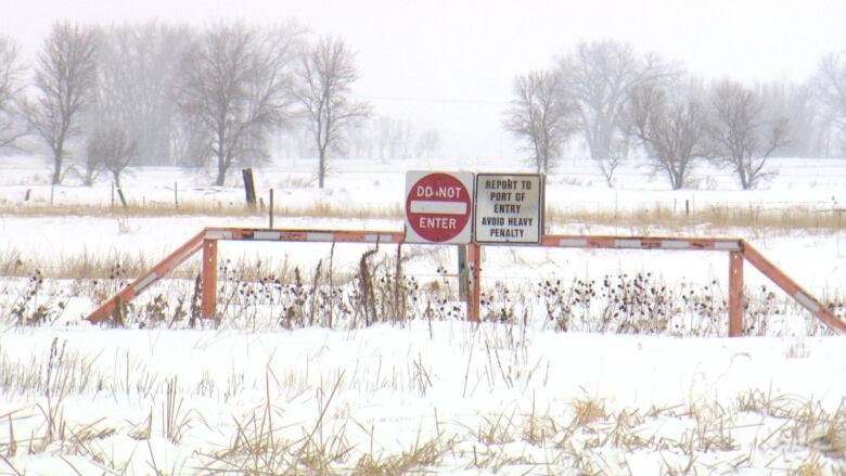 Signs reading 'do not enter' and 'report to port of entry avoid heavy penalty' sit attached to a large sawhorse-shaped structure near the Canada-U.S. border.