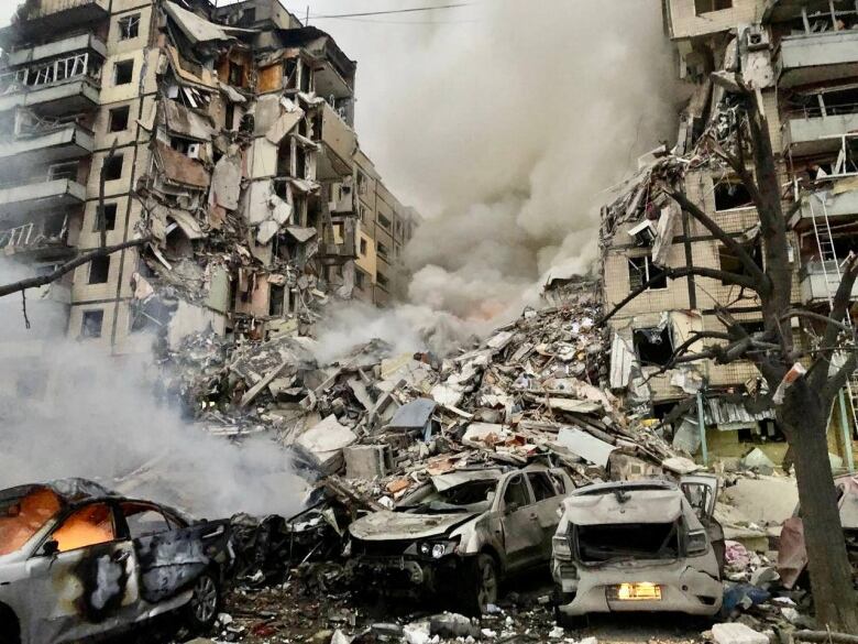 A demolished apartment building with destroyed cars in the forefront.