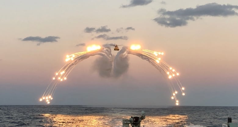 A military helicopter flying over the ocean launches flares.