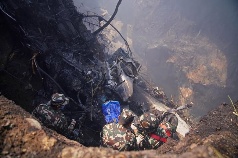 Men look down at plane wreckage at the side of a gorge.