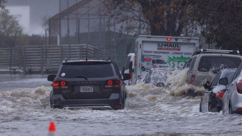 A car driving through a flooded street splashes water against parked cars. 