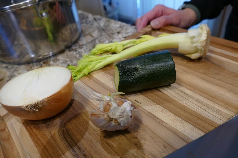 Half an onion, a partial stock of celery, some garlic and a piece of zucchini sitting on a cutting board in a kitchen.