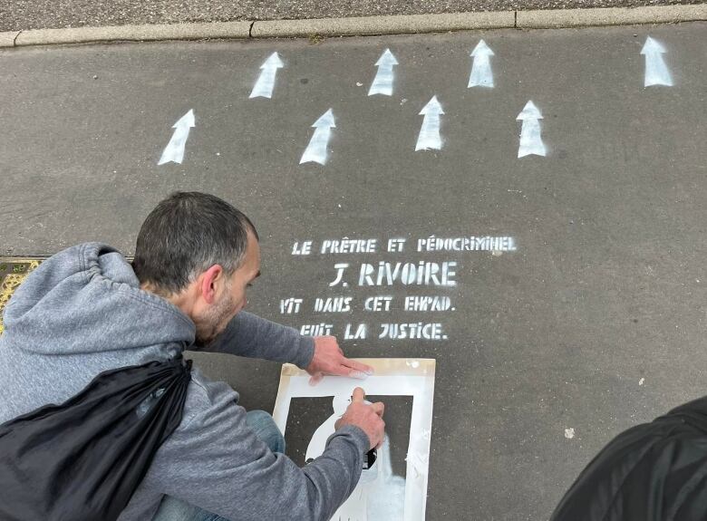 A man uses spray paint to paint a figure and message on a road.