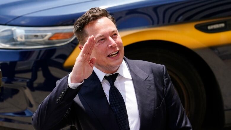 A man in a suit waves to unidentified persons in an outdoor setting.