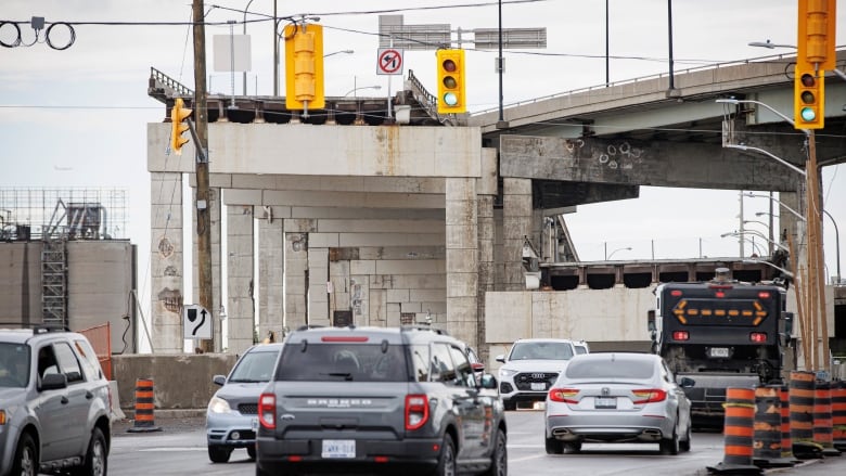 Multiple cars are pictured navigating a road with construction cones and a sign.