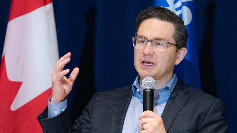 Conservative Leader Pierre Poilievre speaks on a stage with a Canadian and a Quebec flag behind him. 