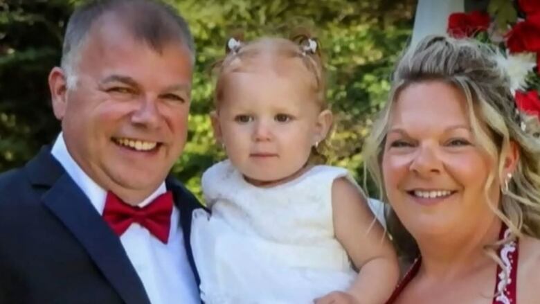 A man and woman in formal clothing hold a little girl.