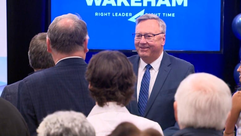 A man wearing a blue suit smiles as he greets a crowd. 