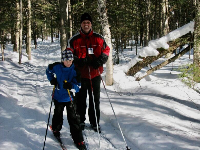 A father and son cross-country skiing in the woods.