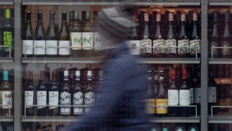 A person walks past shelves of bottles of alcohol on display.