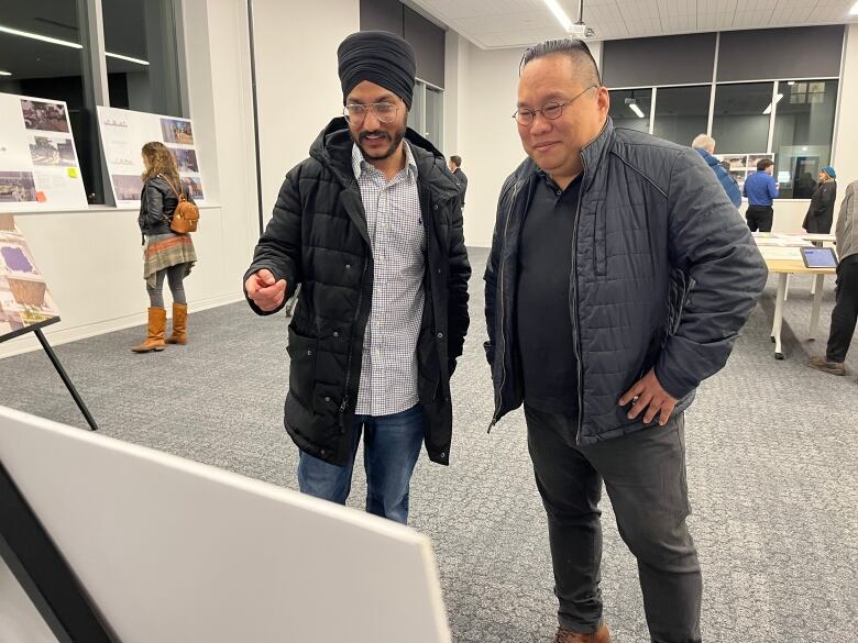 Two men look at a billboard in a brightly lit room. 