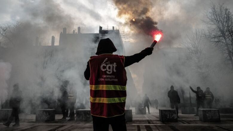 A man stands holding a flare during a demonstration in France.