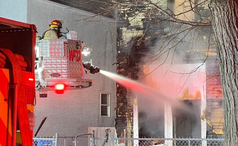 A firefighter at the left of the photograph sprays water from a hose into a burning house.