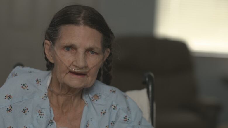 A woman in a hospital gown with an oxygen tube along her face is looking off camera. She looks quite sickly. 