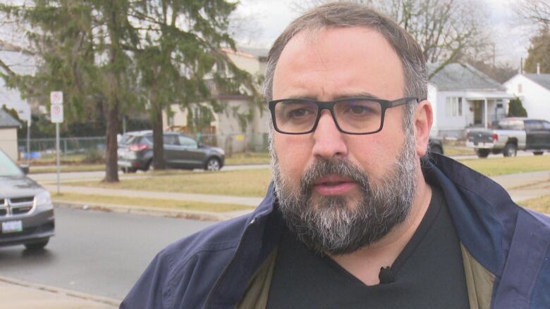 A bearded man with glasses on a street corner.