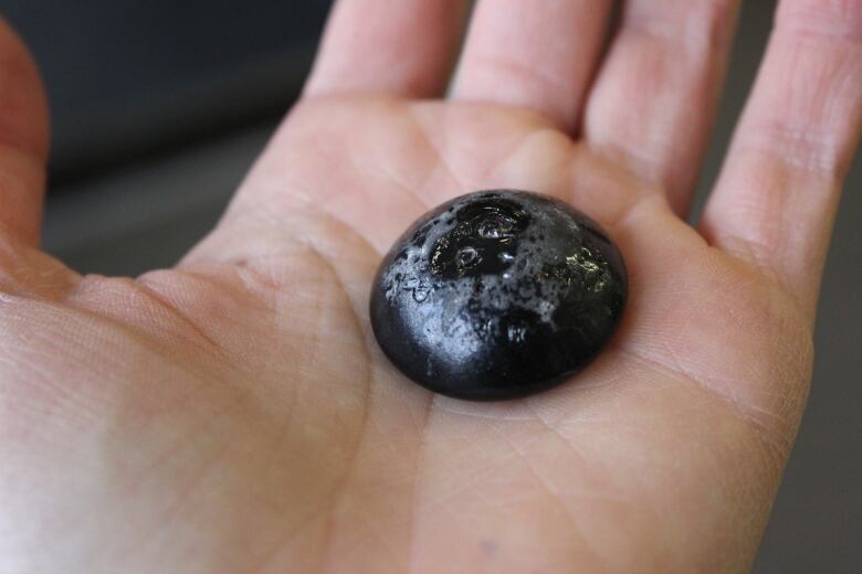 A black pebble in a white person's hand. 