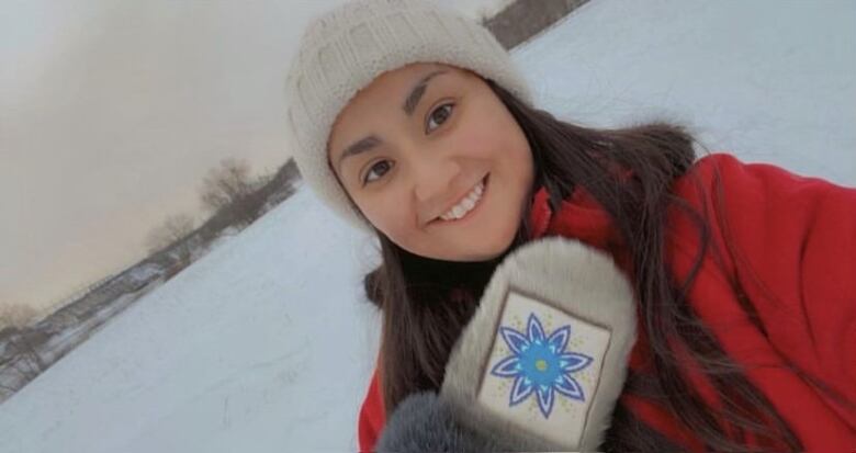 An Indigenous woman with a red jacket and toque takes a selfie in the snow. 