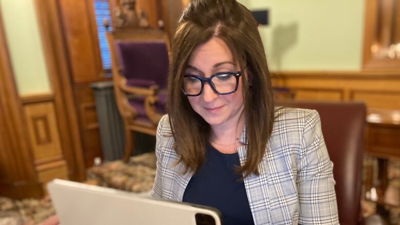 A woman sits at a table in front of a laptop computer in the new Brunswick legislature.