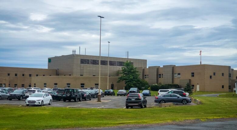 A view of a hospital, with a parking lot full of cars next to it.