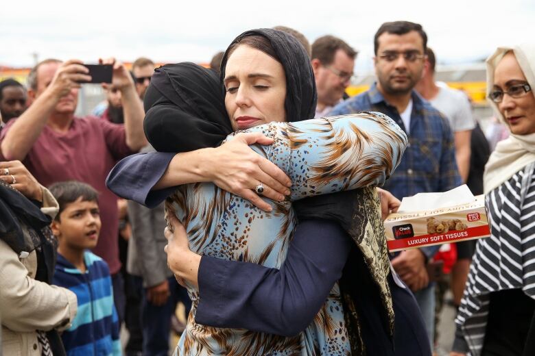 Two women in headscarves embrace in a crowd of people. 