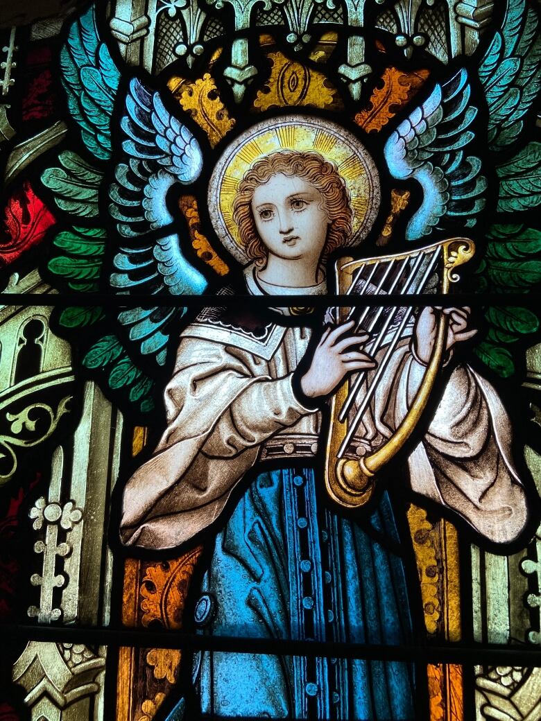 Stained glass featuring an angel holding an instrument. 