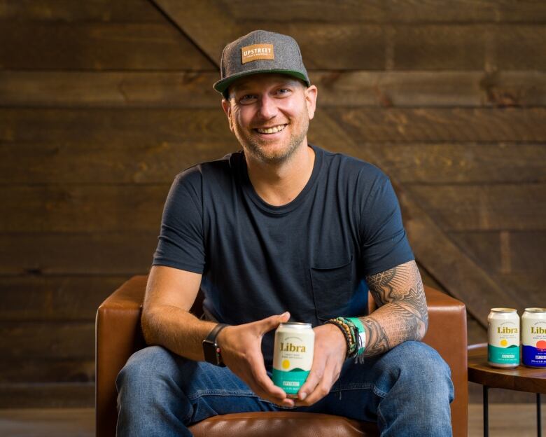 Mitch Cobb sitting on a chair holding a can of his non-alcoholic drink, Libra. 