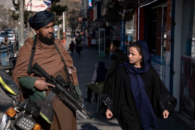 A man holds a gun as a woman walks past on a street.