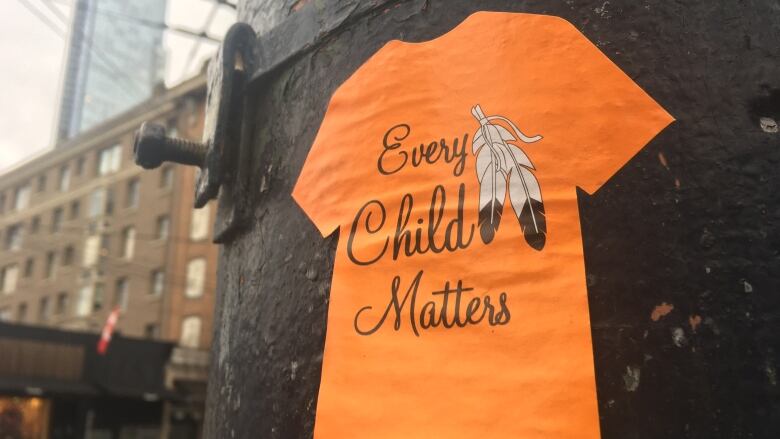 A sticker of an orange t-shirt with the words 'Every Child Matters' on it affixed to a lamp post.