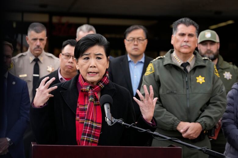 A congressional representative speaks into a microphone beside police officials. 