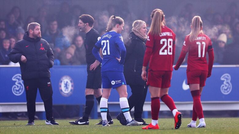 A soccer referee interacts with players and coaches in the field as members of the audience watch on from the back.