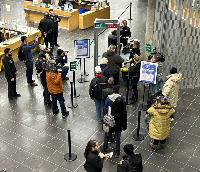 A lineup of people, seen from above, wait to enter a metal detector to enter a library.