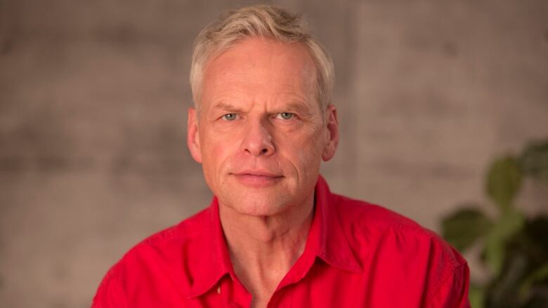 A blond man with a red shirt looks into the camera.