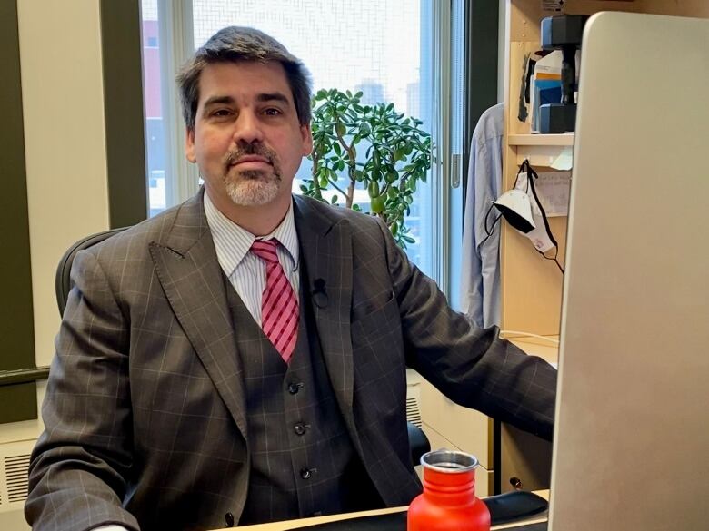 A man in a suit smiles at a desk.