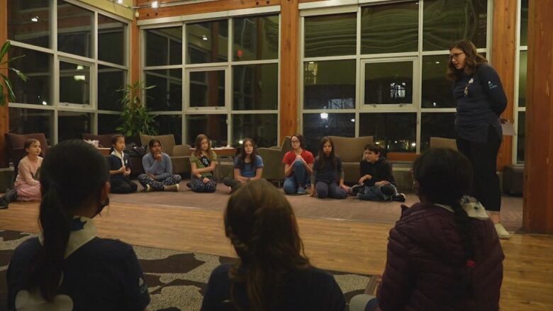 A group of Girl Guides sit in a circle on a carpeted floor.