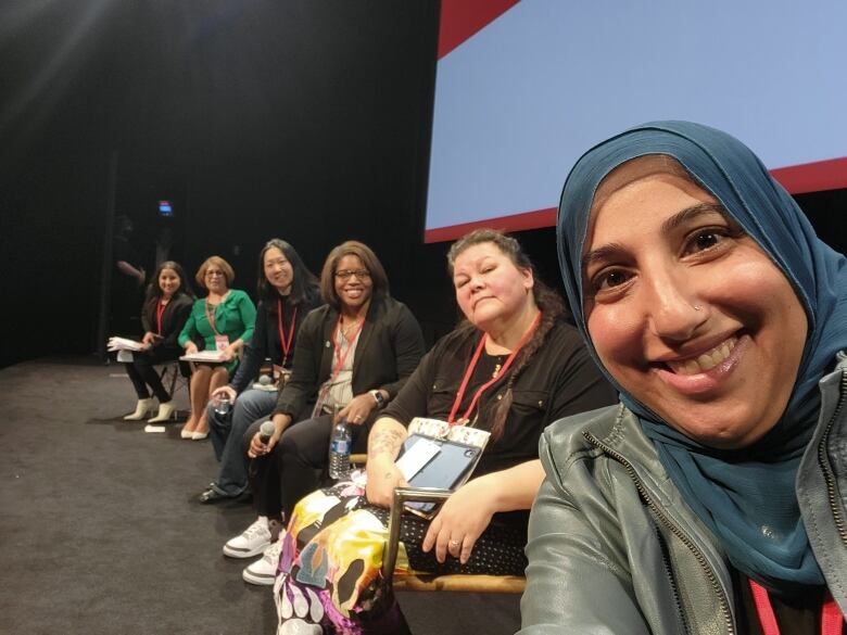 Six women sit on a stage.