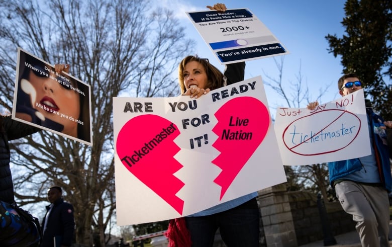 People stand outdoors holding banners calling for the break-up of Ticketmaster and Live Nation.