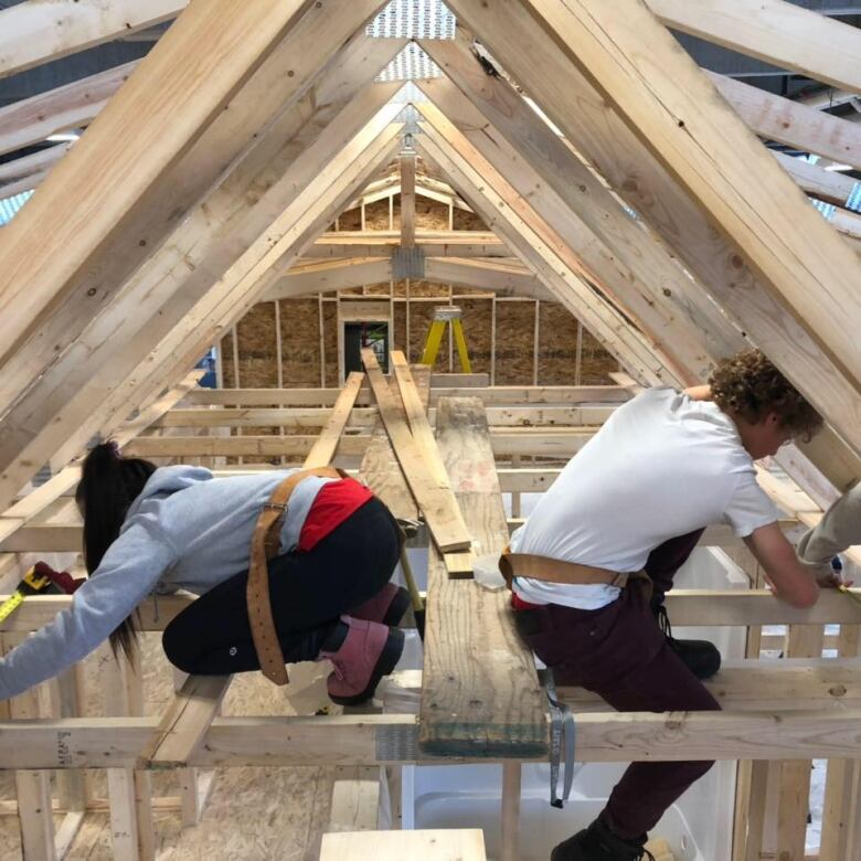 A man and a woman are bent over pieces of wood. They are working on the roof of the house frame.  