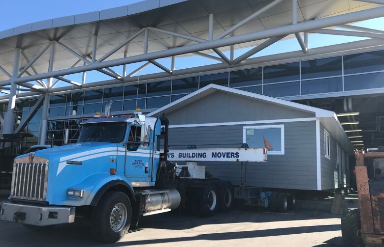 Grey house sits on the back of a large moving truck.